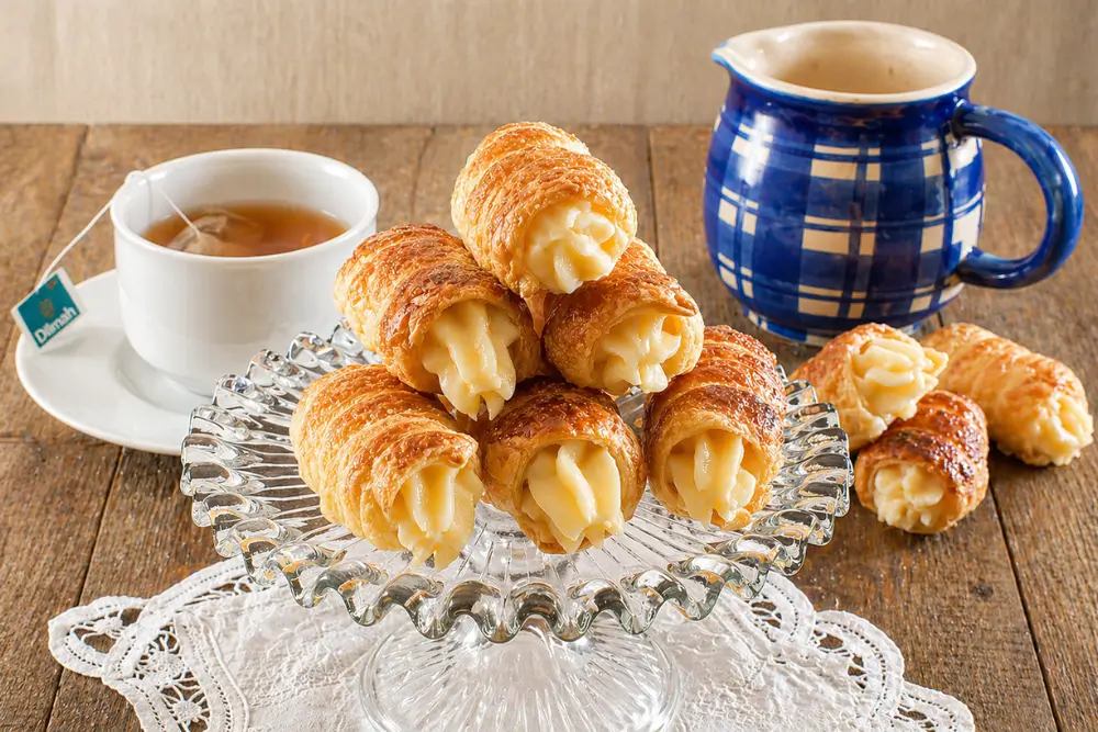 Golden puff pastry cannoncini served with hot tea and a blue ceramic coffee pot.