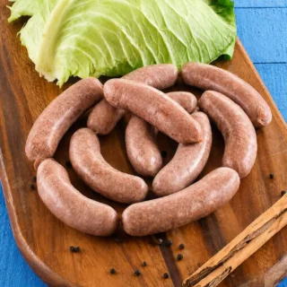 Homemade Verzini sausages arranged on a wooden board with fresh cabbage leaves and whole peppercorns.