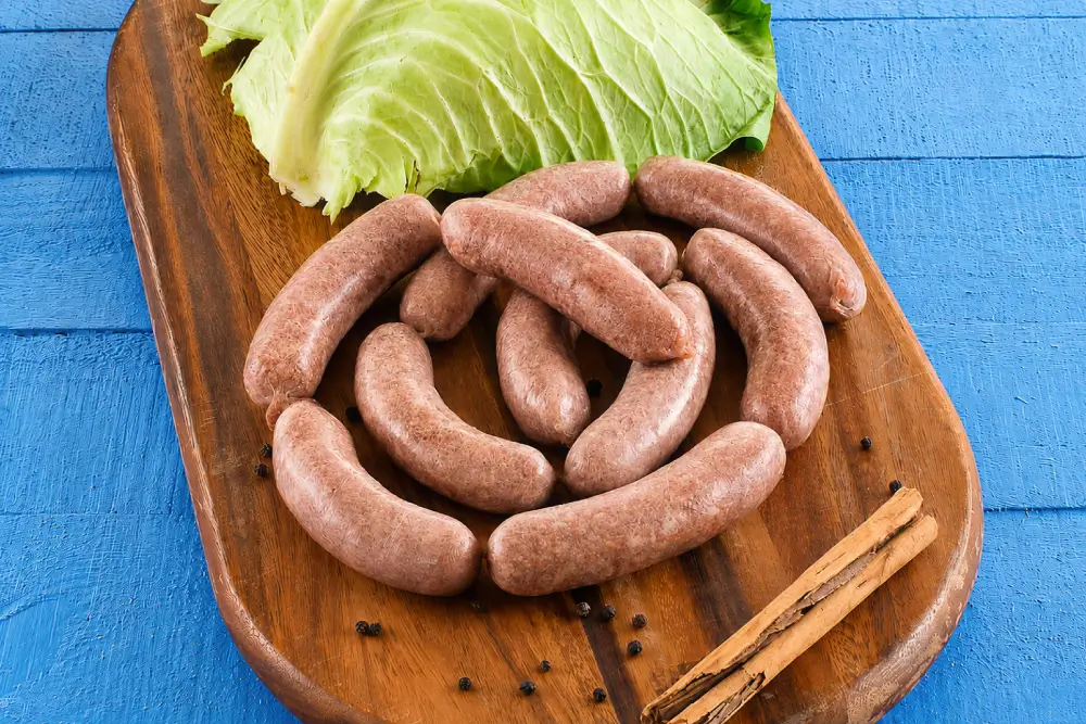 Homemade Verzini sausages arranged on a wooden board with fresh cabbage leaves and whole peppercorns.