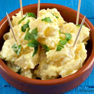 Creamy Patatas Alioli served in a bowl with aioli and garlic cloves nearby.