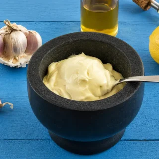 Spoon lifting thick and creamy homemade aioli from a black serving bowl.