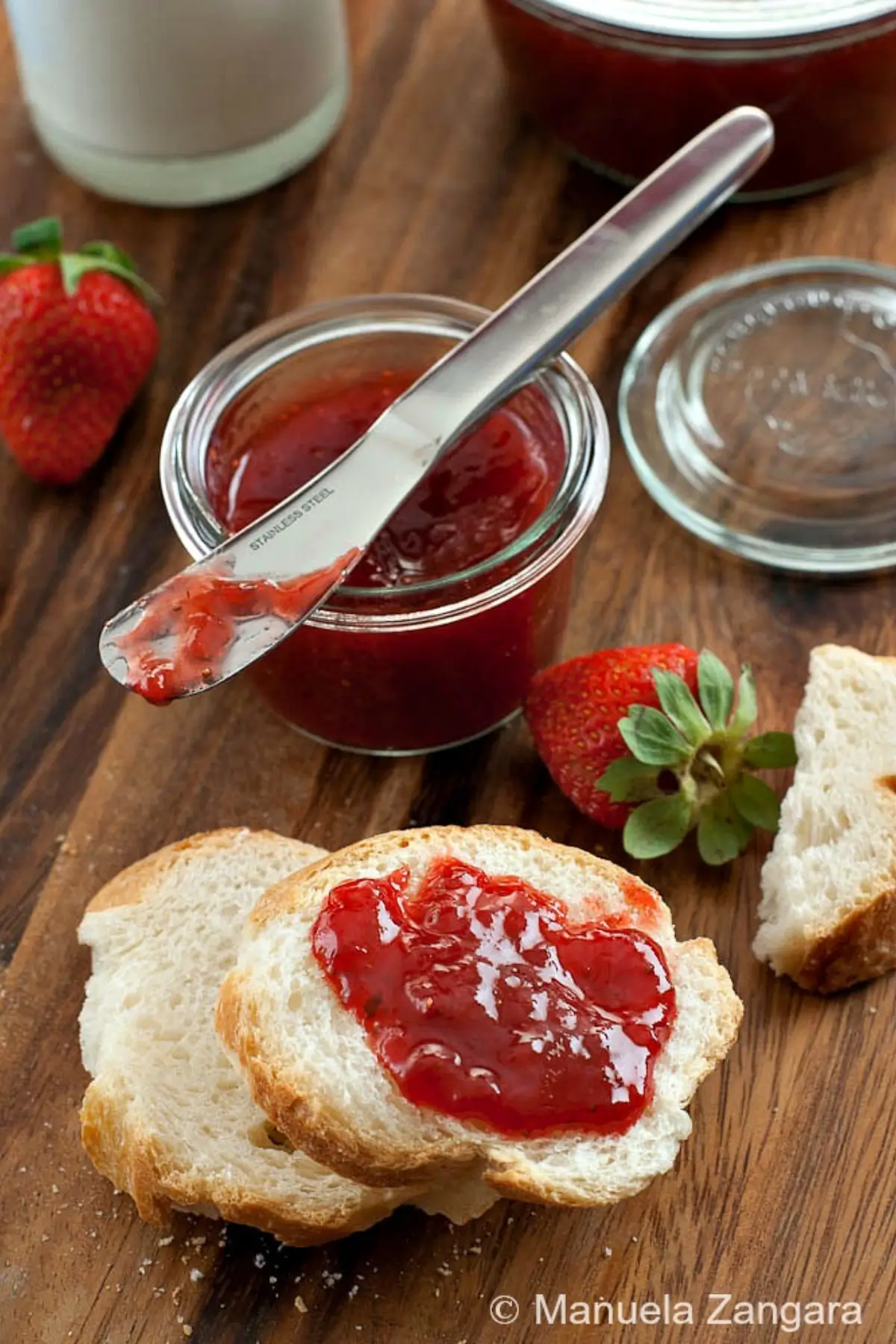 Glossy strawberry spread on sliced bread with whole fresh strawberries.
