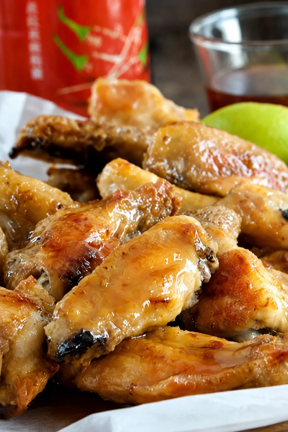 Crispy glazed chicken wings served on baking paper over a wooden board.