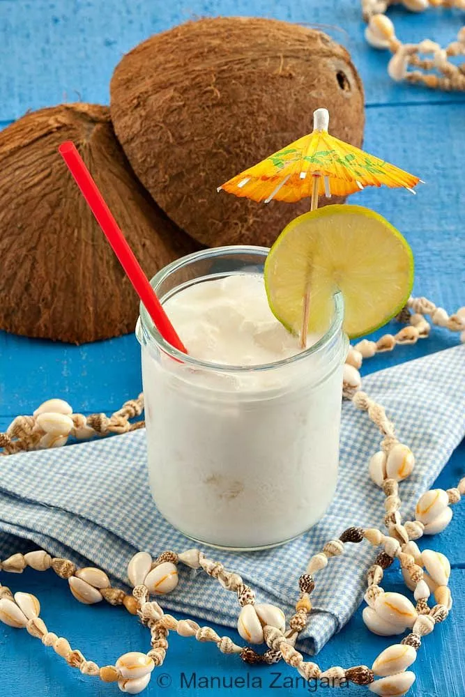 Creamy coconut cocktail served in a glass jar with lime, straw, and paper umbrella.