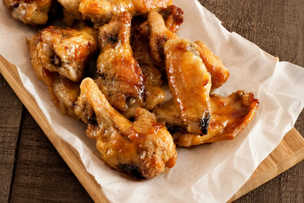 Close-up of baked chicken wings coated in a glossy maple and sriracha glaze with lime in the background.