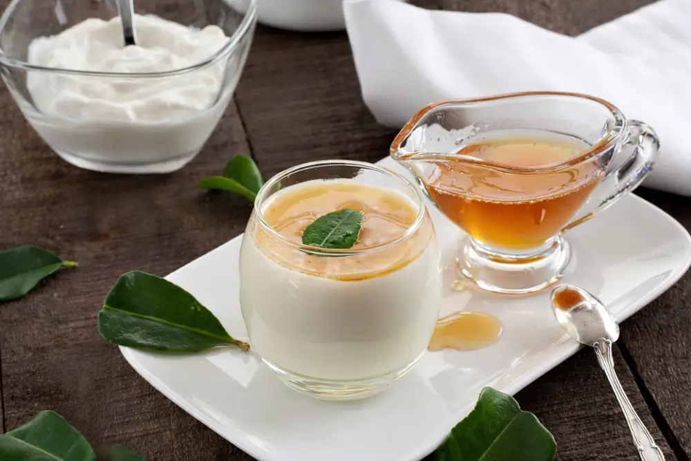 Creamy panna cotta topped with honey and a fresh leaf garnish on a white plate.