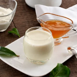 Set panna cotta in a glass on a white plate with honey and a spoon on the side.