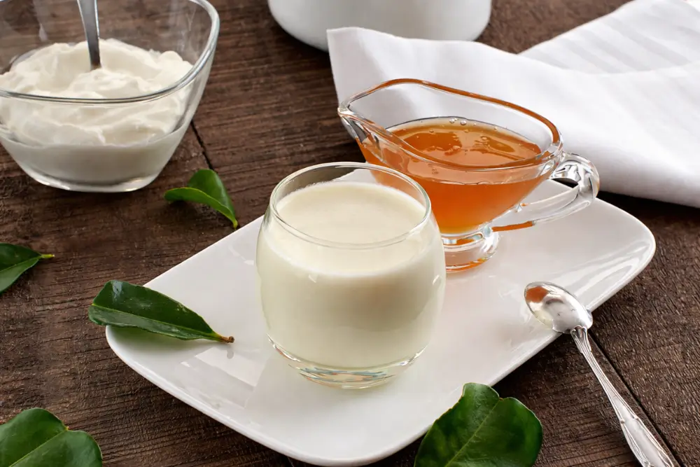 Set panna cotta in a glass on a white plate with honey and a spoon on the side.