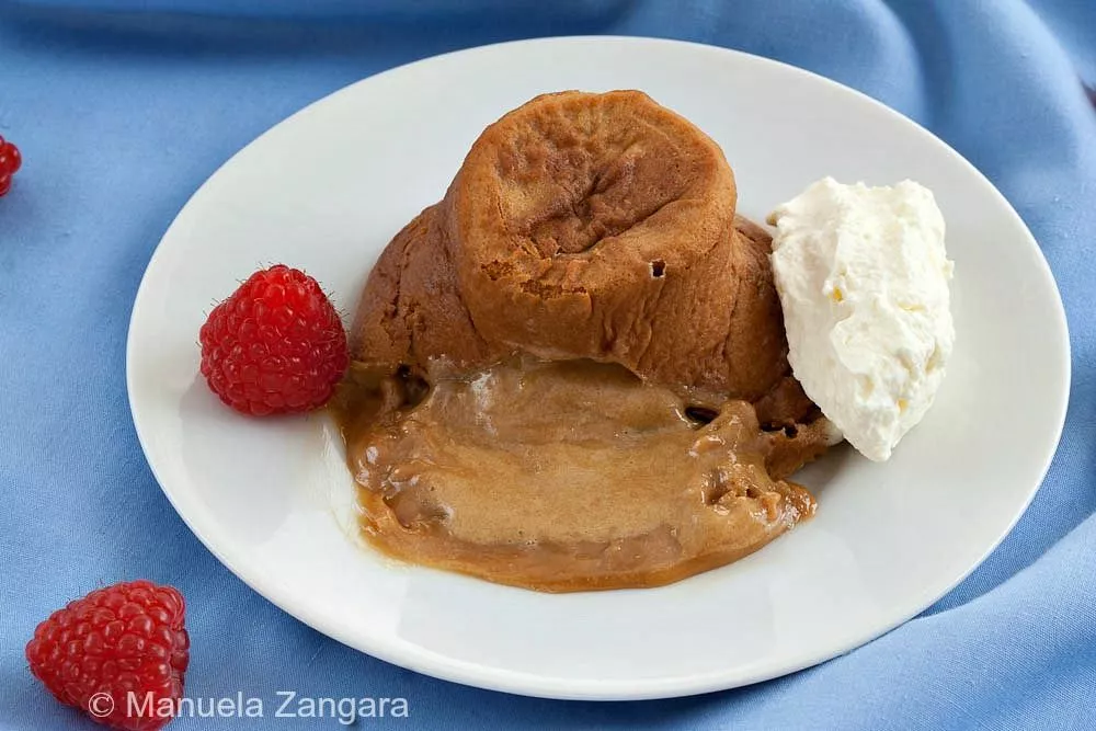 Molten dulce de leche cake served with fresh raspberries and a scoop of whipped cream on a blue tablecloth.