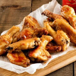Sticky glazed chicken wings arranged on baking paper over a wooden serving board.
