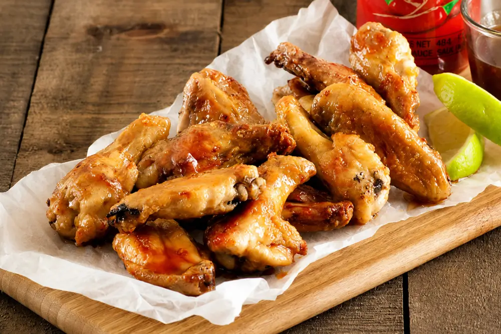 Sticky glazed chicken wings arranged on baking paper over a wooden serving board.