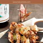 Yakitori chicken skewers with spring onions glazed in sauce, served on a black plate with dipping sauce.