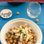 Bowl of Salada de Bacalhau e Grão with salted cod, chickpeas, red onion, and parsley served on a blue table.