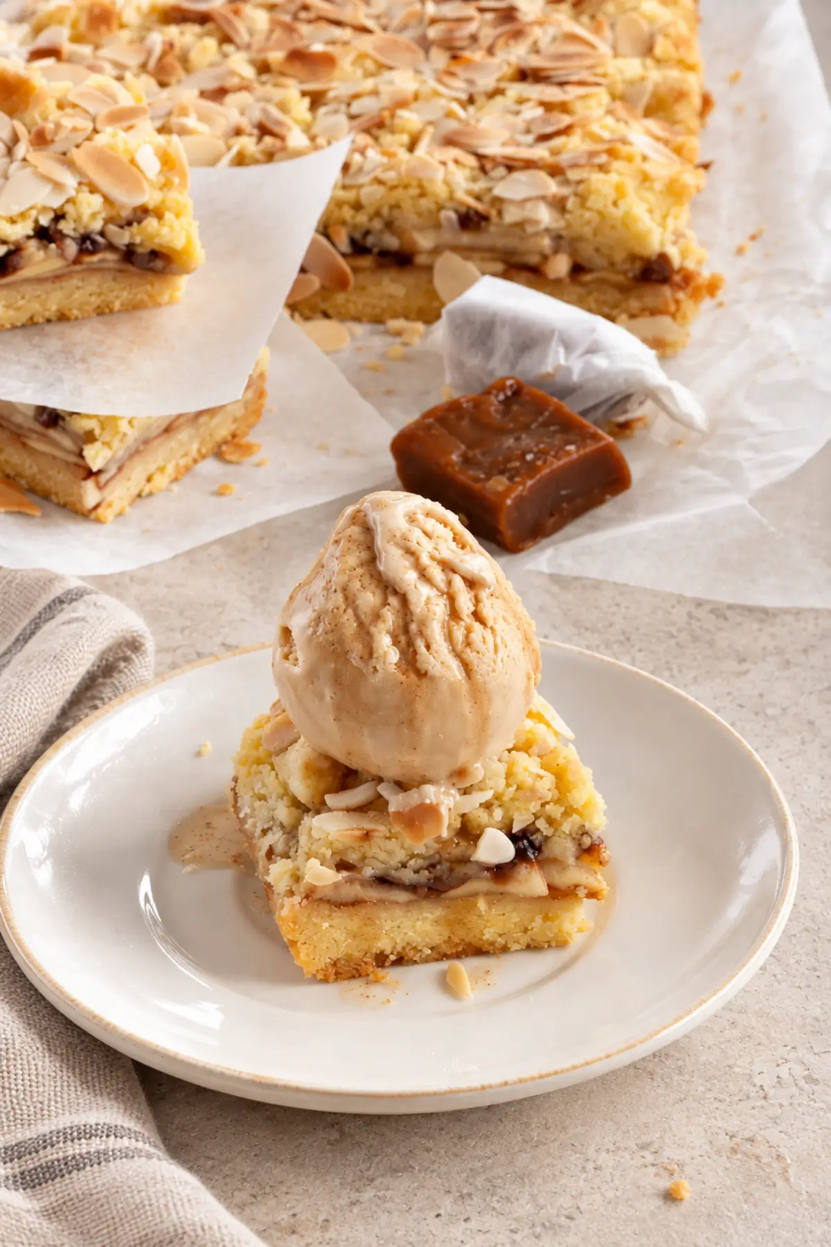 Apple crumble bar topped with a scoop of caramel gelato and served on a white plate.