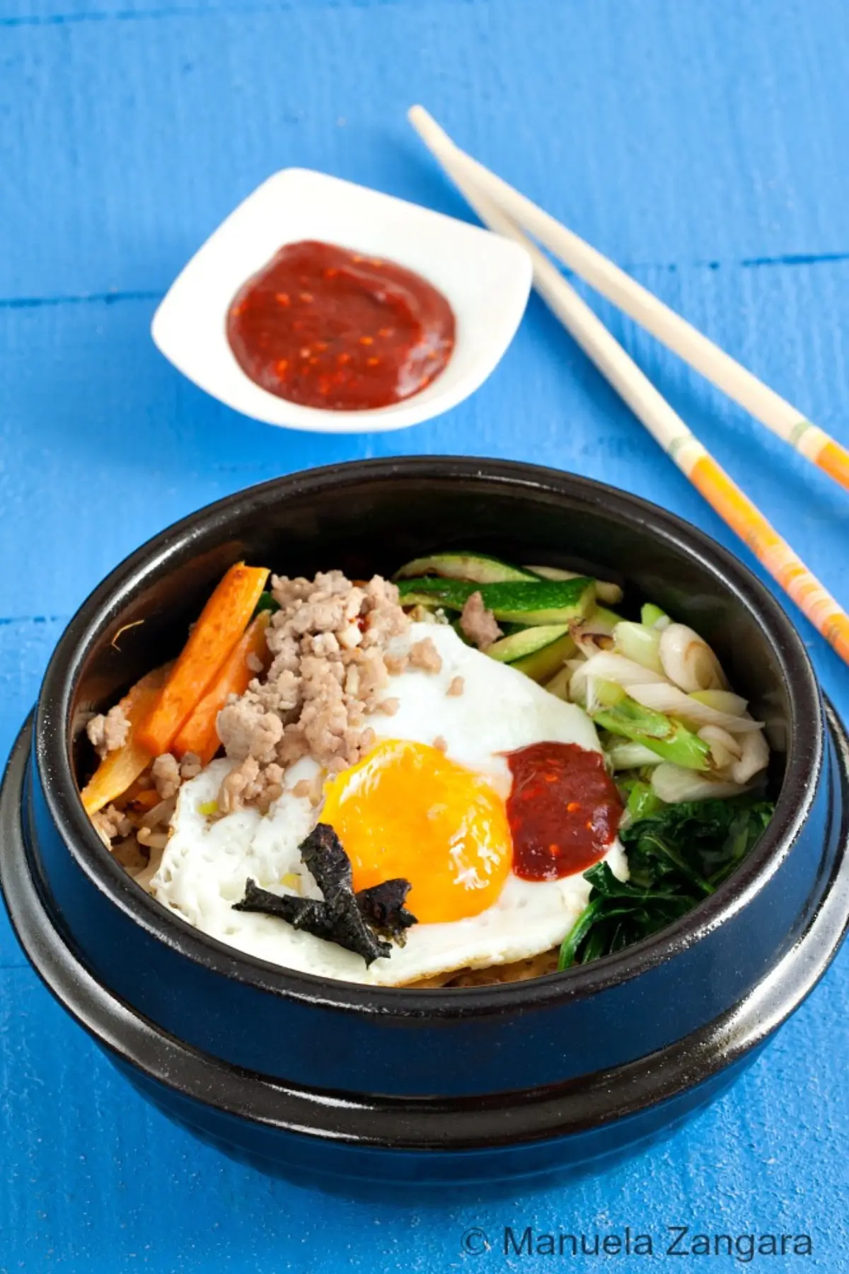Bibimbap served in a stone bowl with egg and vegetables.