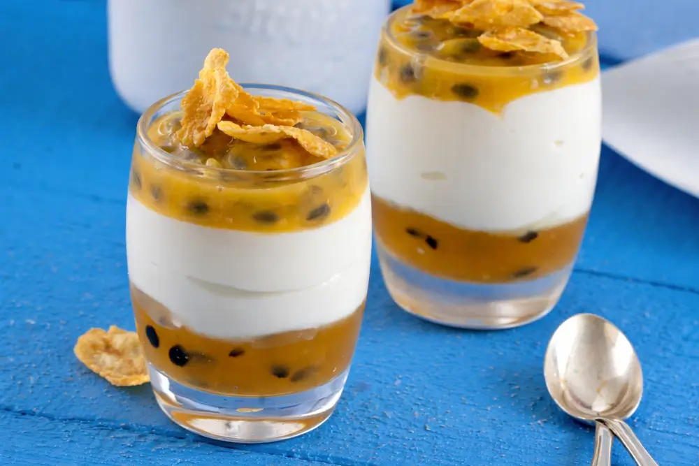 Layered yoghurt and passion fruit in a glass, finished with cornflakes on top.