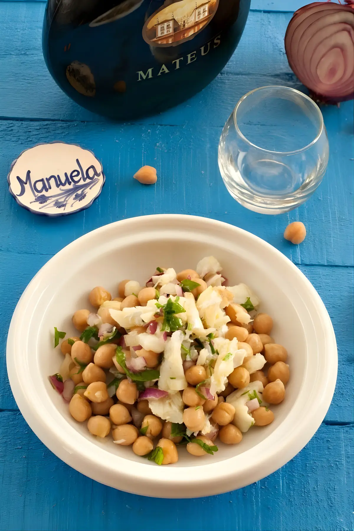 Overhead view of Salada de Bacalhau e Grão served in a white bowl with a glass and bottle of Mateus wine in the background