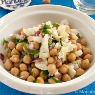 Bowl of Salada de Bacalhau e Grão with salted cod, chickpeas, red onion, and parsley served on a blue table.