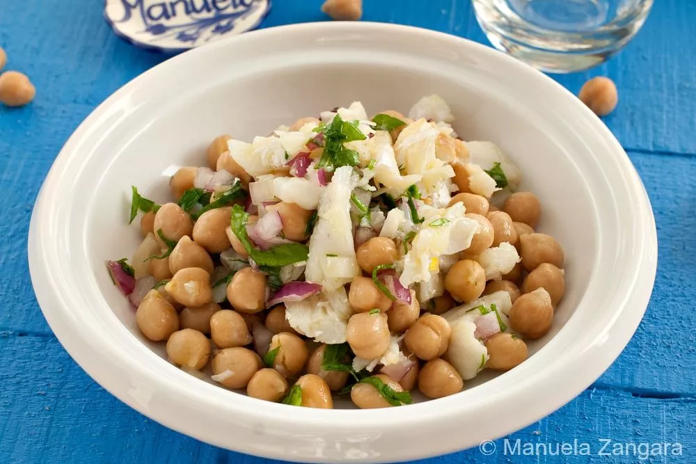 Bowl of Salada de Bacalhau e Grão with salted cod, chickpeas, red onion, and parsley served on a blue table.
