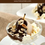 Poire belle Hélène with chocolate sauce, whipped cream, and almonds, presented in a glass dish.