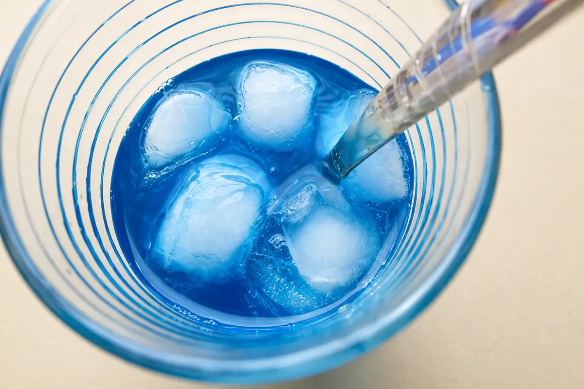 Overhead view of a bright blue cocktail with ice cubes.