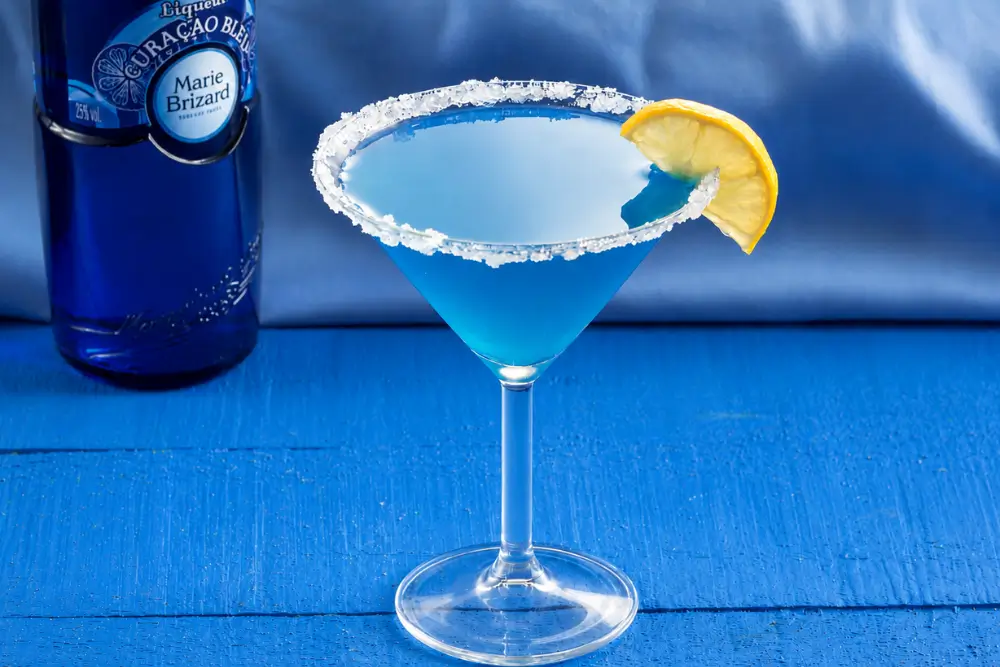 Blue Daiquiri cocktail beside a bottle of Blue Curaçao liqueur.
