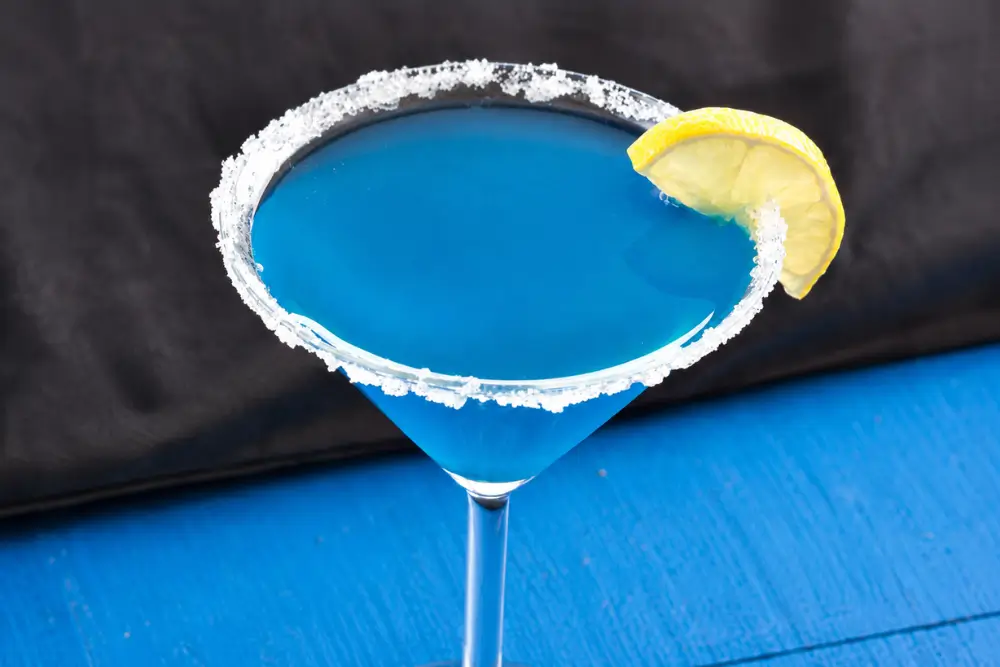 Side view of a bright blue rum cocktail in a sugar-rimmed Martini glass.