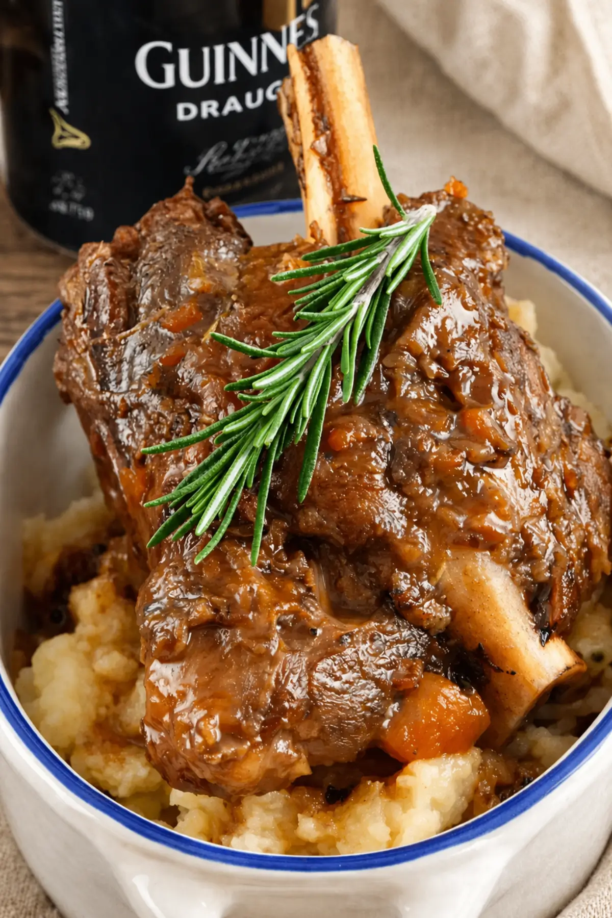 Close-up of a braised lamb shank topped with fresh rosemary and rich gravy.
