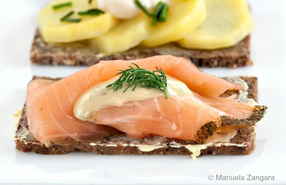 Close-up of salmon Smørrebrød with dill mustard sauce and fresh dill on rye bread.