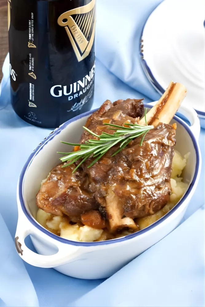 Guinness braised lamb shank served in a small white dish beside a Guinness bottle.