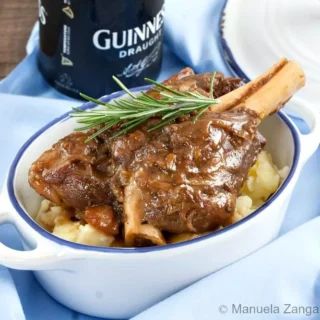 Close-up of Guinness braised lamb shank over creamy mashed potatoes, garnished with rosemary.