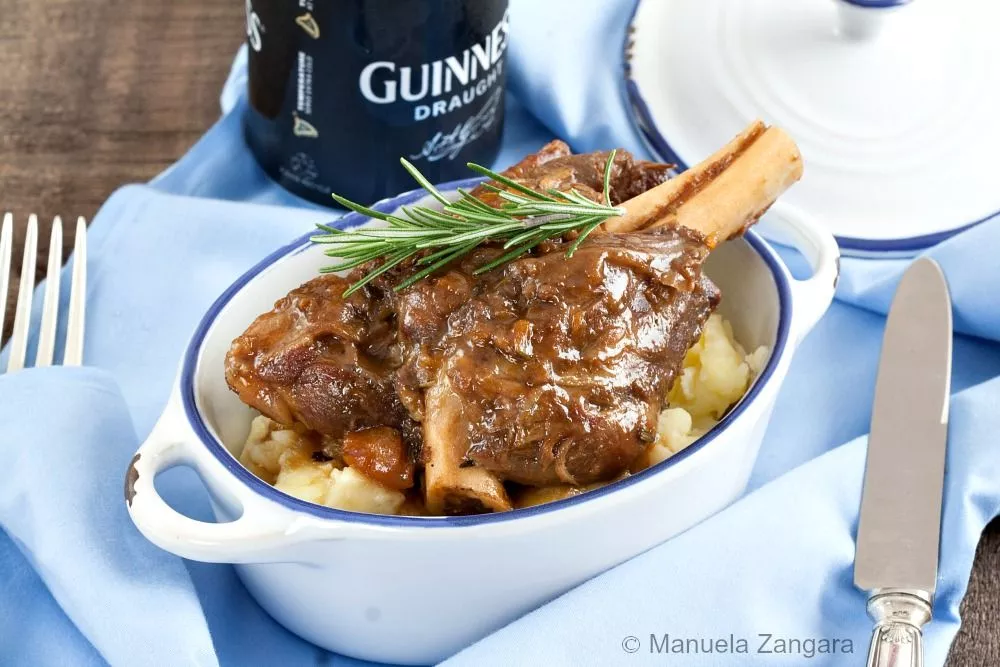Close-up of Guinness braised lamb shank over creamy mashed potatoes, garnished with rosemary.