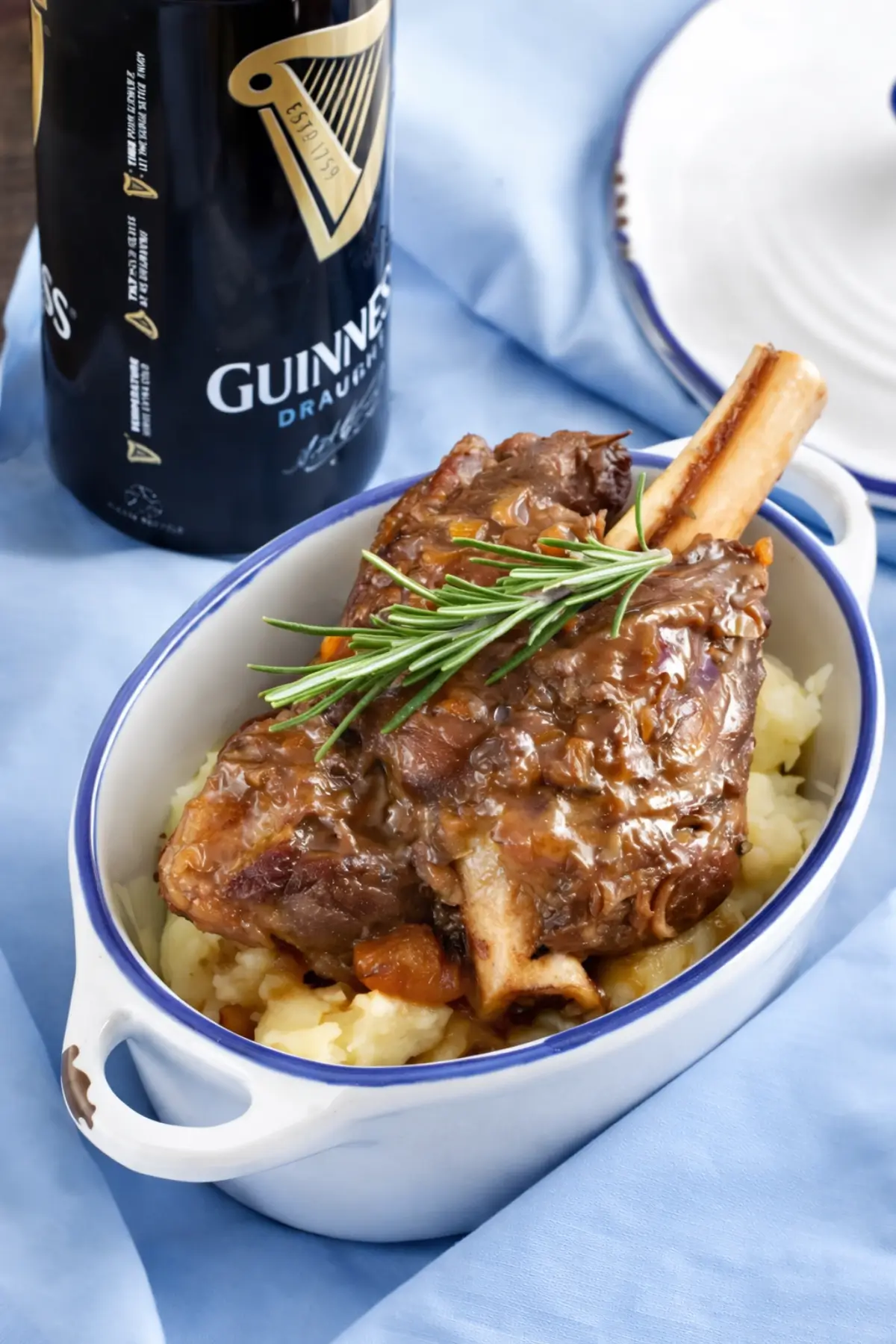 Guinness braised lamb shank served in a small white dish beside a Guinness bottle.