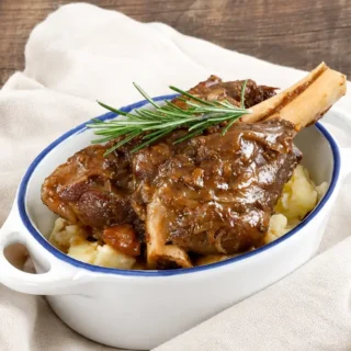 Guinness lamb shanks served over creamy mashed potatoes with rosemary garnish.