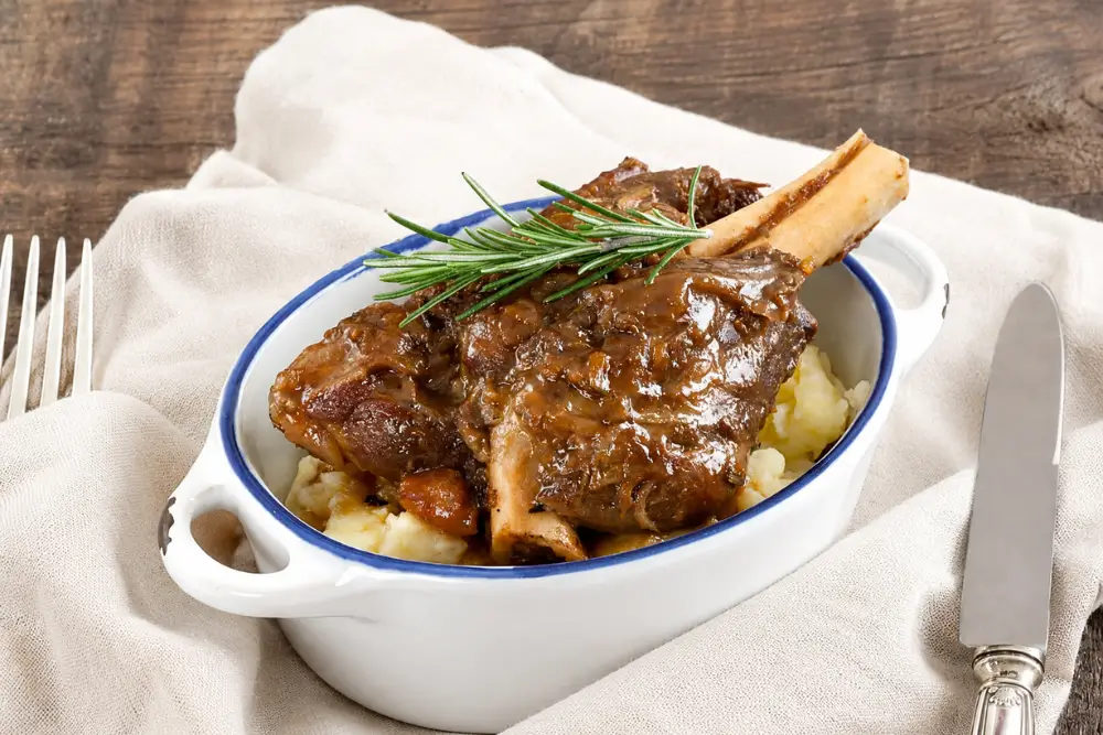 Guinness lamb shanks served over creamy mashed potatoes with rosemary garnish.