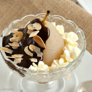 A full view of Poire belle Hélène with chocolate sauce, whipped cream, and almonds, presented in a glass dish.