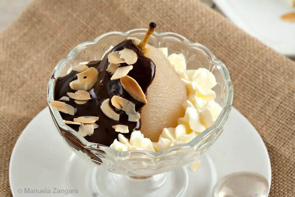 A full view of Poire belle Hélène with chocolate sauce, whipped cream, and almonds, presented in a glass dish.