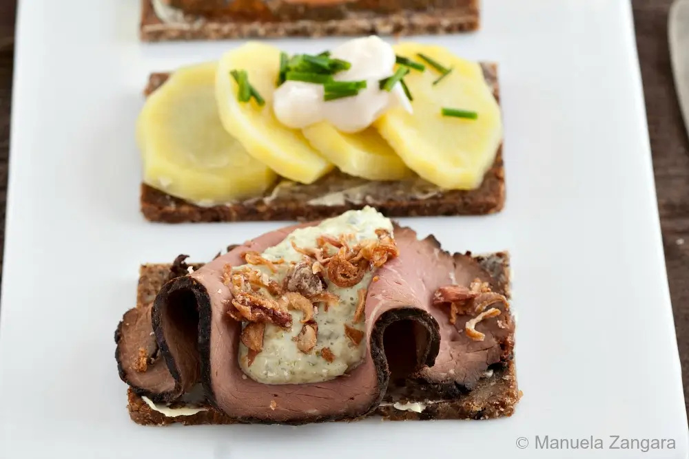 Close-up of roast beef Smørrebrød topped with creamy Remoulade and crispy onions.