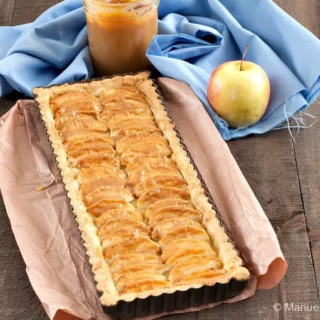 Baked Apple and Dulce de Leche Tart on brown paper with a jar of caramel and an apple beside it.