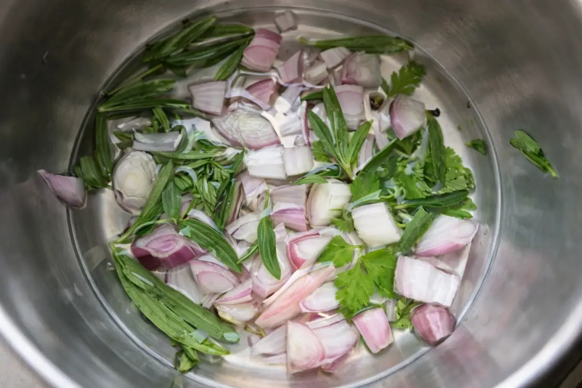 Chopped shallots and fresh herbs soaking in water in a pot.