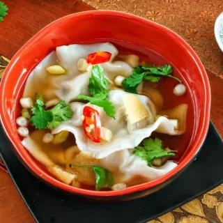 Red bowl filled with dumplings in ginger broth.