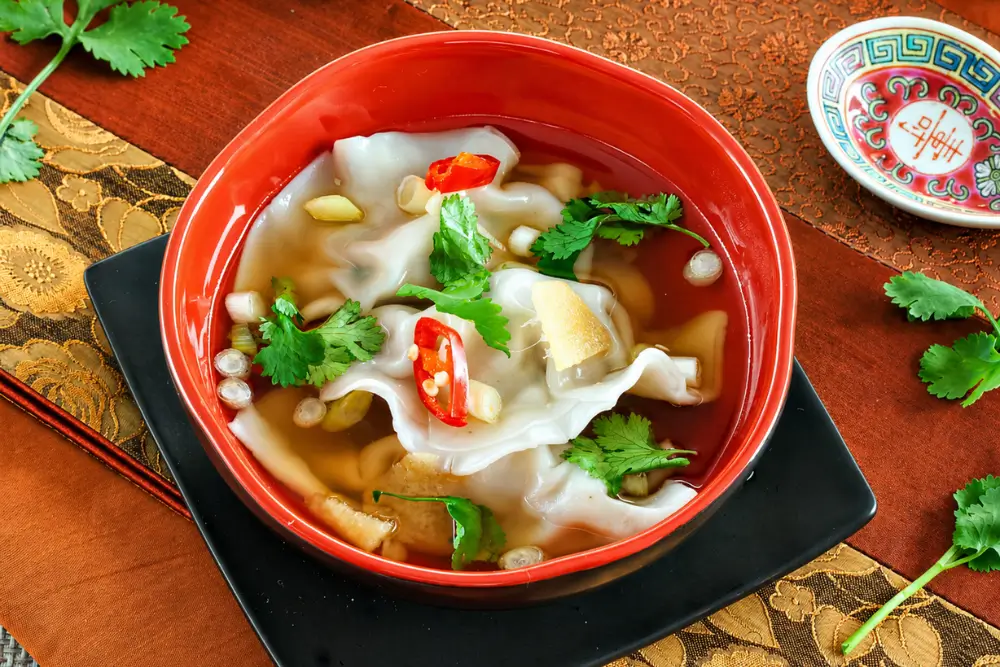Red bowl filled with dumplings in ginger broth.