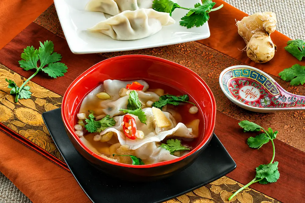 Bowl of momos served in ginger broth with coriander, spring onions, and sliced chilli.