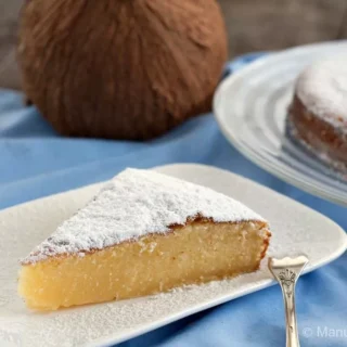 Slice of moist condensed milk and coconut cake topped with icing sugar on a white plate.