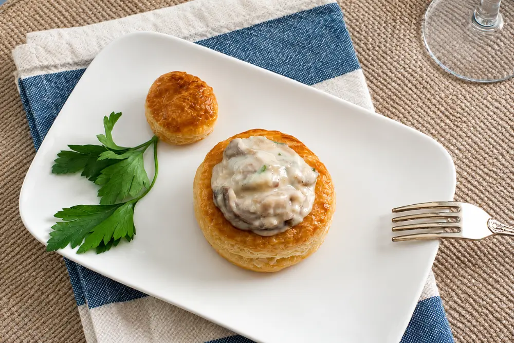 Golden vol au vent filled with creamy mushroom sauce and served with parsley on a white plate.