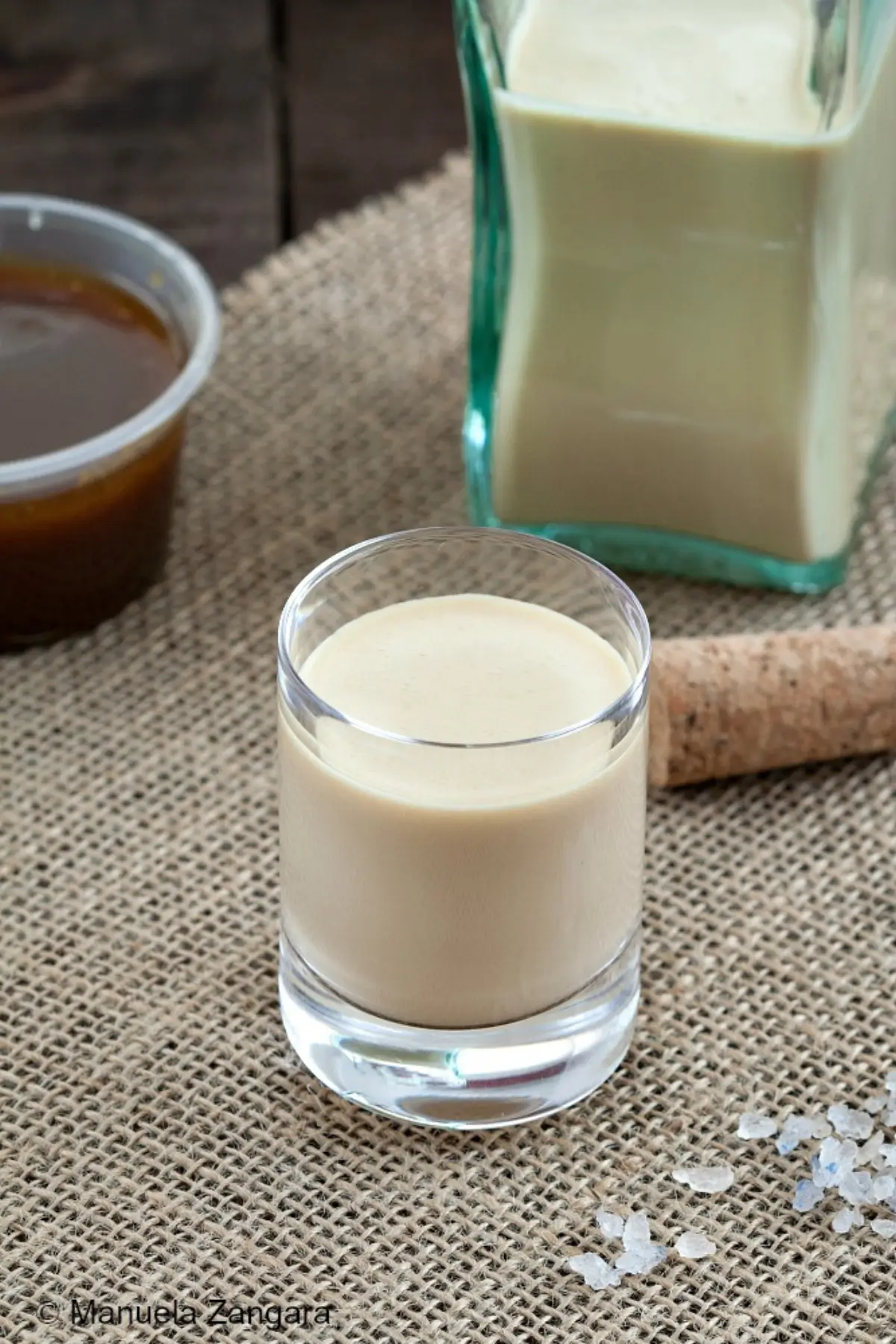 Small glass of creamy salted caramel liqueur with the bottle and caramel sauce on burlap.