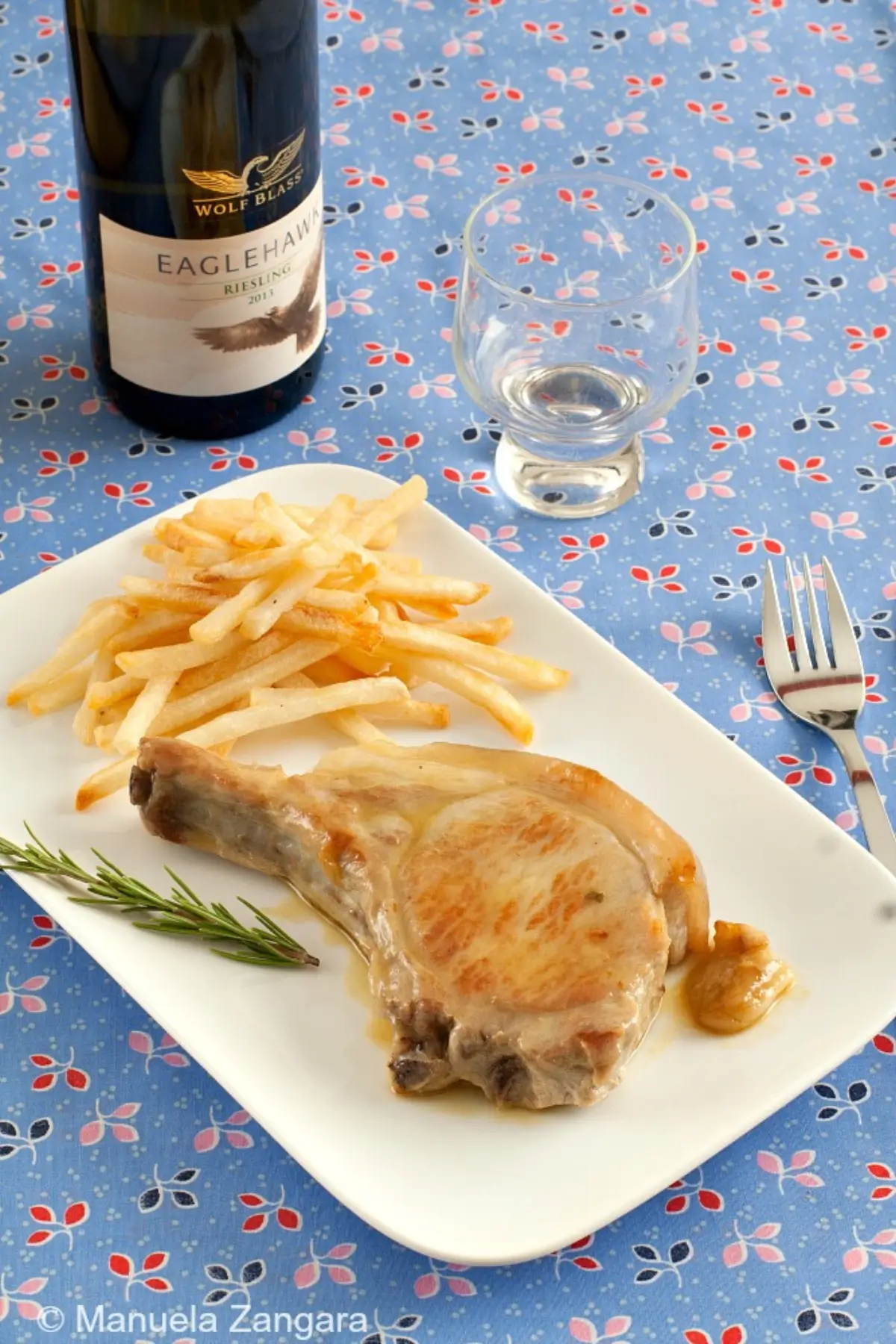 Golden pork chop served with fries, rosemary, and white wine on a table.