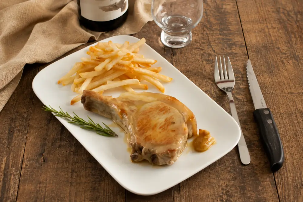 Pork loin cutlet with fries and rosemary on a white rectangular plate.