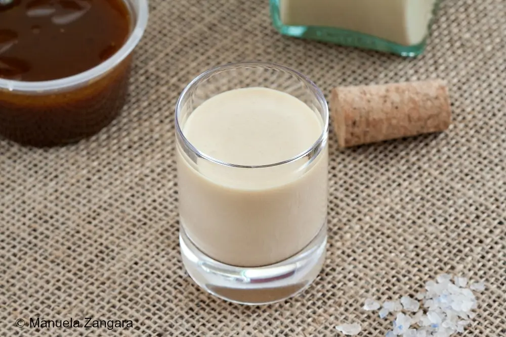 Small glass of homemade salted caramel liqueur with the bottle and caramel sauce on burlap.
