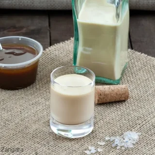 Glass of salted caramel liqueur with jar of caramel sauce and bottle in the background.
